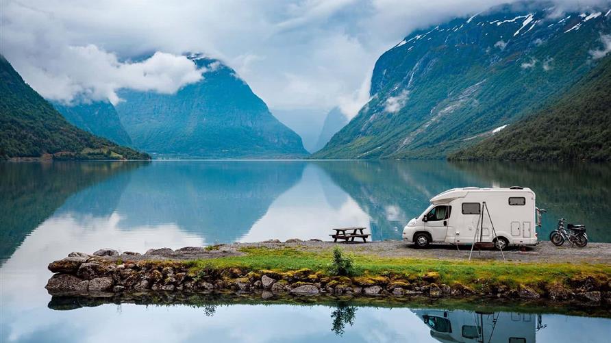 Picture of an RV next to a lake with the mountains in the distance. 