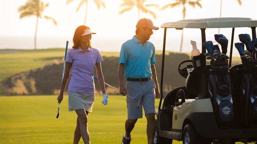 Couple walking on a golf course in Hawaii while on vacation with Hilton Grand Vacations. 