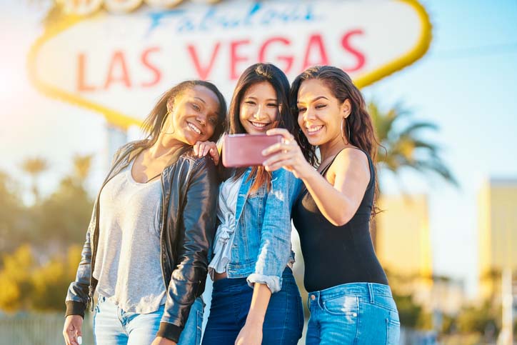 Three girlfriends posing in front the Las Vegas sign on a Hilton Grand Vacations girls' weekend in Las Vegas, Nevada. 