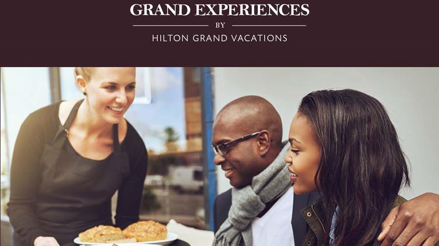 Waitress serving a couple dining out with the Hilton Grand Vacations Grand Experiences card. 