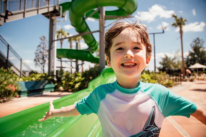 Young boy smiling at the bottom of the waterslide at a Hilton Grand Vacations resort. 