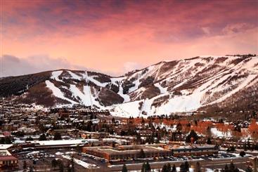 Aerial shot of Park City, Utah with snowcapped mountains against pink painted sunset skies overhead.