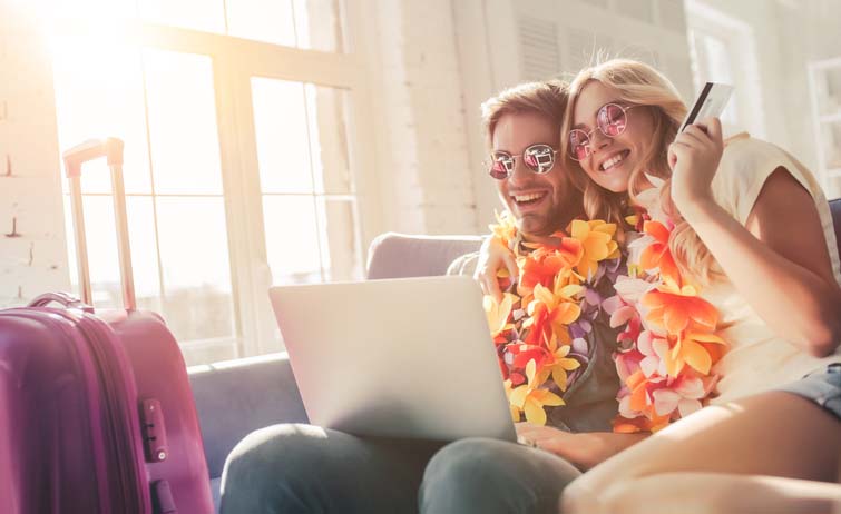 A happy couple wearing leis on their couch booking travel. 
