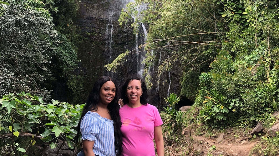 Hilton Grand Vacations Owner and her daughter posing in front of a waterfall on vacation in Hawaii. 