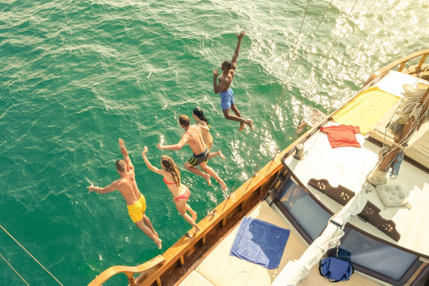 Five people jumping off a boat into the green ocean water