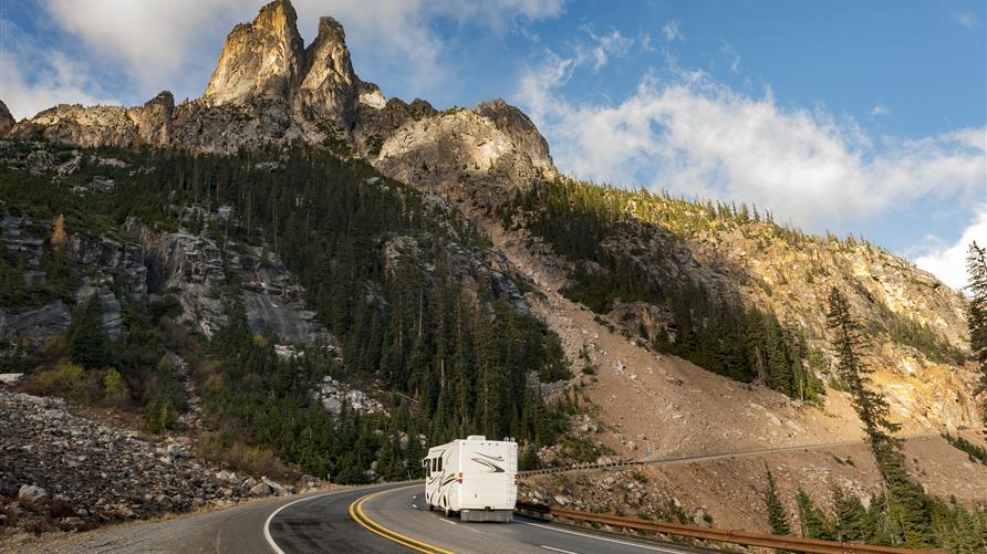 RV driving alongside a mountain.