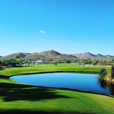 A glassy pond sits in a vibrant golfing green with the Arizona mountains in the background. 