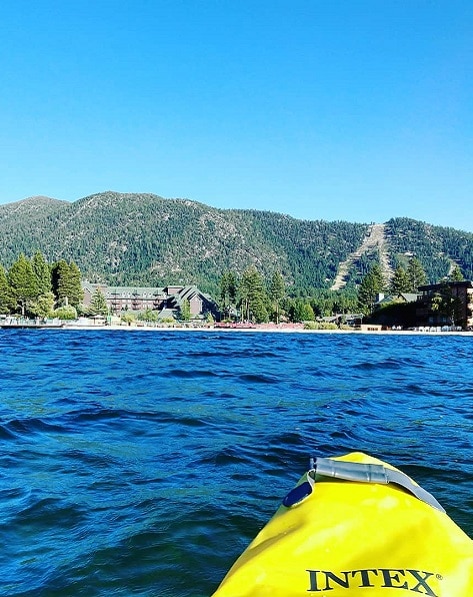 A kayak cuts across the blue waters of Lake Tahoe towards the green mountains of California