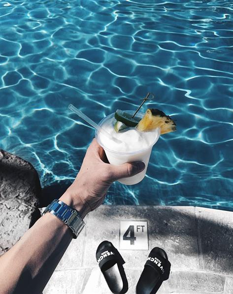 Person holding a mixed cocktail in front of a pool.