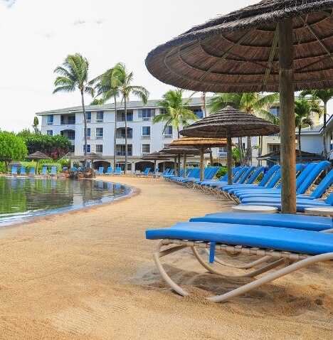 Bright blue beach chairs sit in sand around the water at The Point at Poipu, a Hilton Vacation Club.