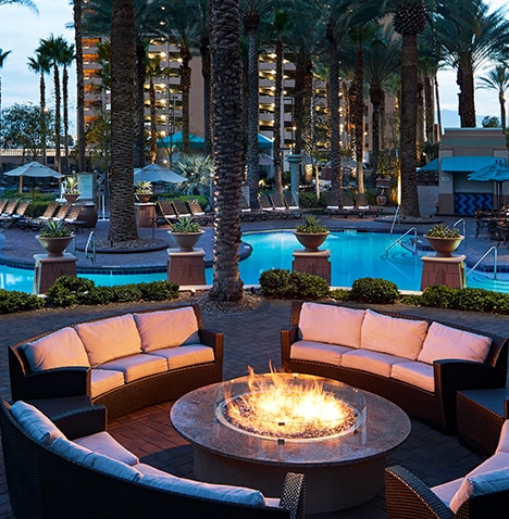 The Boulevard, a Hilton Grand Vacations Club | Sofas arranged around a fireplace with the Boulevard resort building and pools in the background