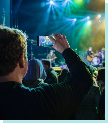 Concert goer taking a photo of a brightly lit stage.