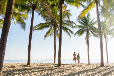 Couple standing under palm trees at the beach.