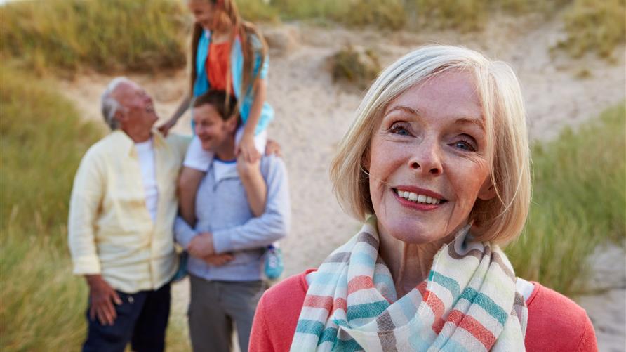 Grandmother smiling at the camera with her husband, son and granddaughter enjoying multigenerational travel in the background.