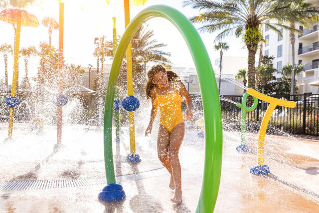 Young girl smiling while playing on the splash pad at Las Palmeras by Hilton Grand Vacations resort in Orlando. 