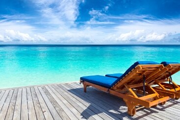 Two beach lounge chairs on a deck overlooking a bright blue ocean.